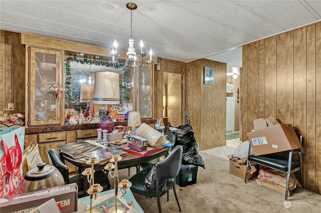 carpeted dining room with wooden walls, a textured ceiling, a chandelier, and visible vents