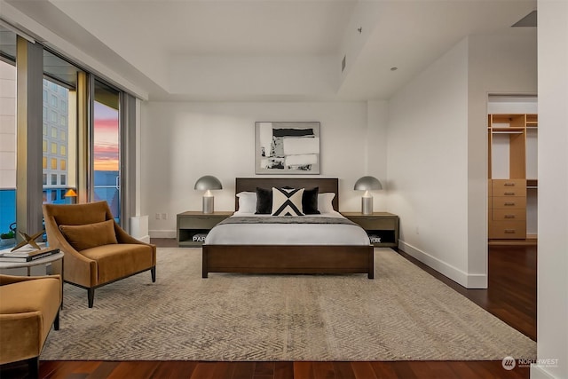 bedroom with dark wood-type flooring, access to outside, and a tray ceiling