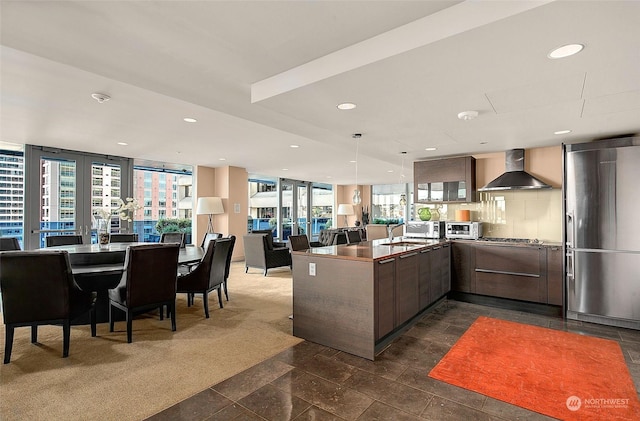 kitchen featuring sink, stainless steel fridge, backsplash, kitchen peninsula, and wall chimney exhaust hood