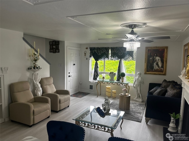 living room with light wood-type flooring, ceiling fan, and a textured ceiling