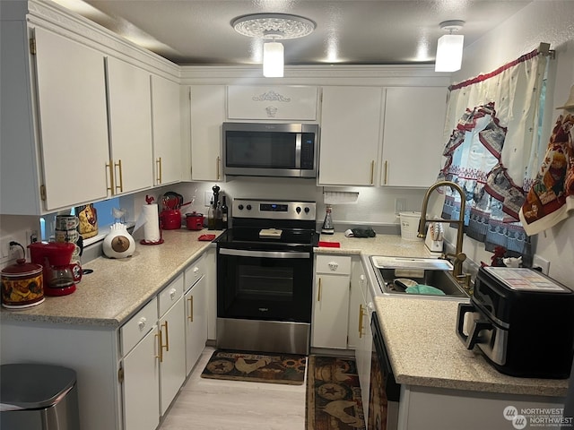 kitchen with appliances with stainless steel finishes, light wood-type flooring, white cabinetry, and sink