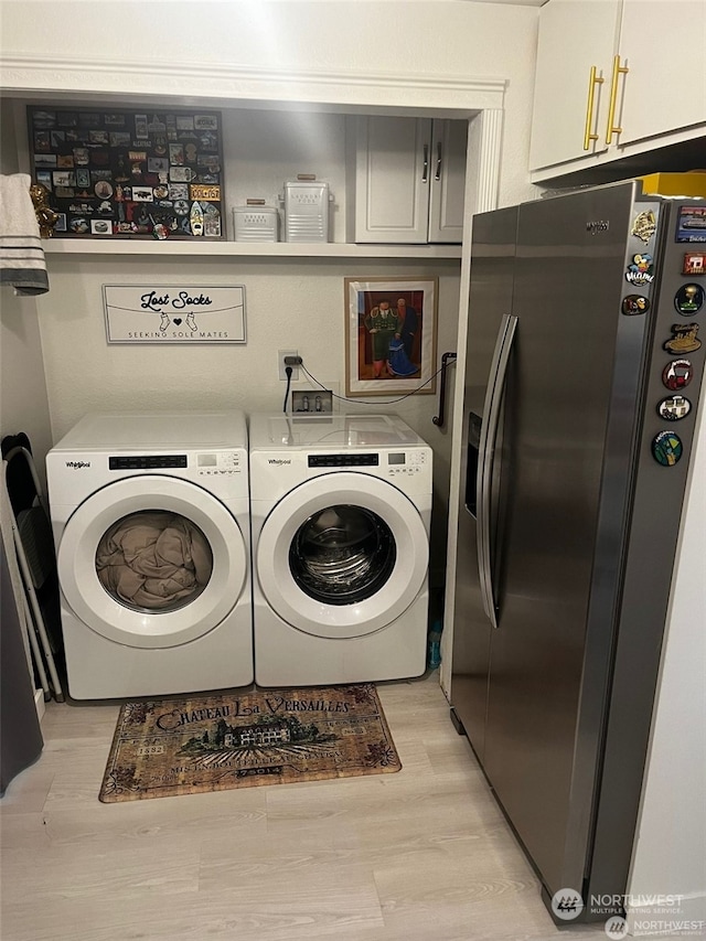 laundry area with light wood-type flooring, washing machine and clothes dryer, and cabinets