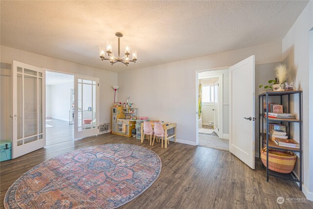 recreation room featuring french doors, a textured ceiling, dark wood-type flooring, and a notable chandelier