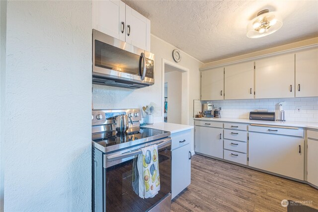 kitchen with a textured ceiling, white cabinetry, decorative backsplash, appliances with stainless steel finishes, and hardwood / wood-style floors