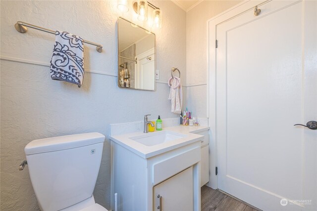 bathroom with wood-type flooring, crown molding, vanity, and toilet