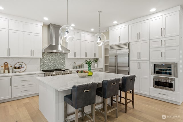 kitchen featuring white cabinets, wall chimney range hood, a kitchen breakfast bar, appliances with stainless steel finishes, and a center island