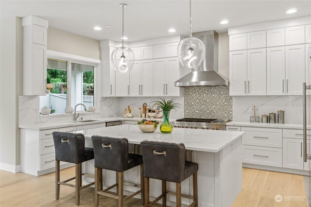 kitchen with white cabinets, hanging light fixtures, a kitchen island, wall chimney exhaust hood, and a kitchen breakfast bar