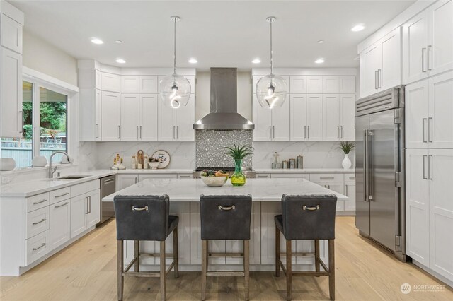 kitchen with stainless steel built in fridge, white cabinets, a center island, and wall chimney range hood