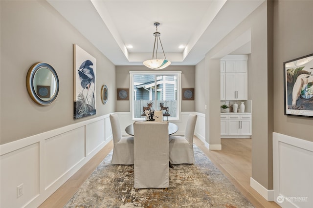 dining space with a raised ceiling and light hardwood / wood-style floors