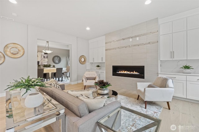 living room with baseboards, visible vents, light wood-type flooring, a fireplace, and recessed lighting