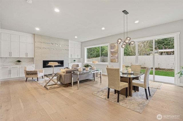 dining area featuring a tile fireplace, a notable chandelier, light wood-style flooring, and recessed lighting