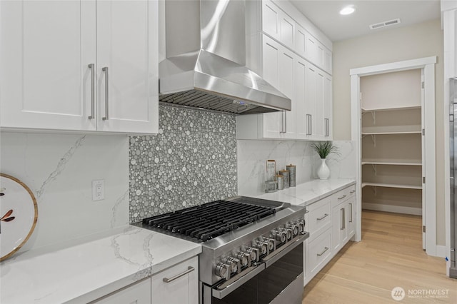 kitchen with light stone countertops, double oven range, white cabinetry, and extractor fan