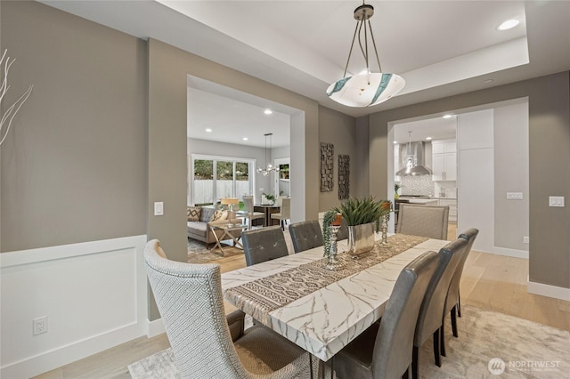 dining room with a tray ceiling, a wainscoted wall, light wood-style flooring, and recessed lighting