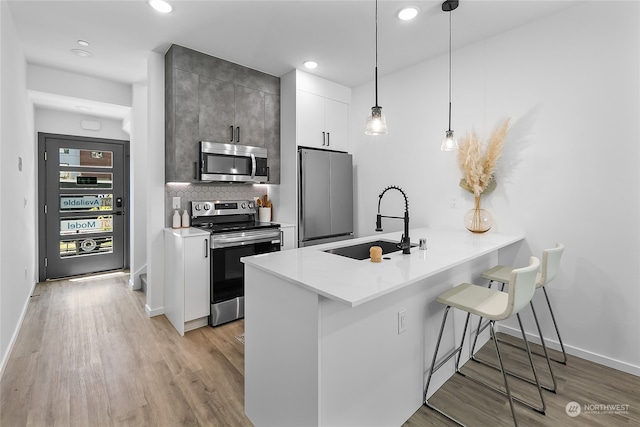 kitchen featuring a kitchen breakfast bar, kitchen peninsula, stainless steel appliances, decorative light fixtures, and white cabinets