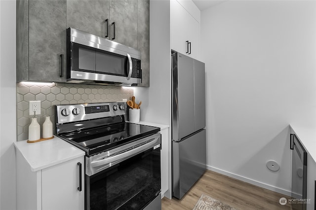 kitchen featuring appliances with stainless steel finishes, white cabinetry, light wood-type flooring, and backsplash