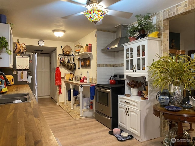 kitchen with light wood finished floors, stainless steel range with electric stovetop, a sink, wall chimney exhaust hood, and ceiling fan