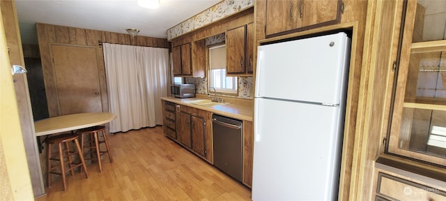 kitchen with appliances with stainless steel finishes, sink, a breakfast bar area, and light hardwood / wood-style flooring