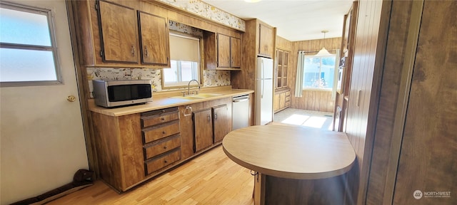 kitchen with sink, appliances with stainless steel finishes, tasteful backsplash, decorative light fixtures, and light wood-type flooring