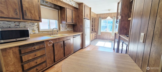 kitchen with sink, light hardwood / wood-style flooring, wooden walls, stainless steel appliances, and decorative light fixtures