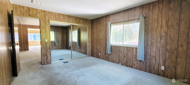 unfurnished bedroom featuring wooden walls, light colored carpet, and a closet