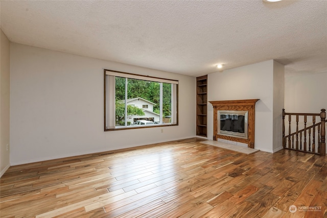 unfurnished living room with light hardwood / wood-style flooring and a textured ceiling