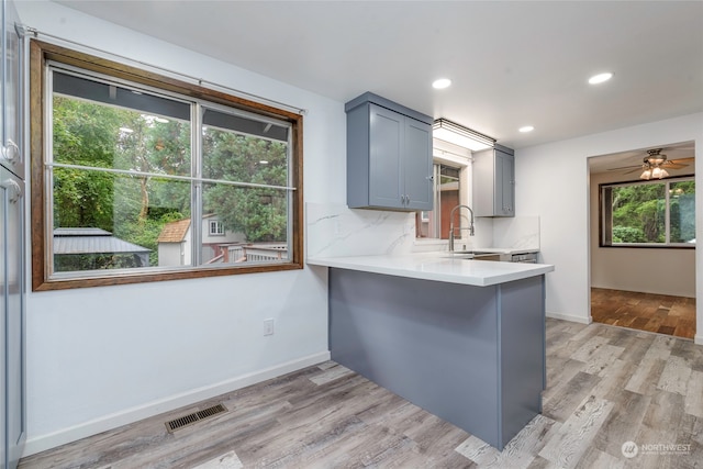 kitchen featuring ceiling fan, sink, kitchen peninsula, light hardwood / wood-style floors, and decorative backsplash