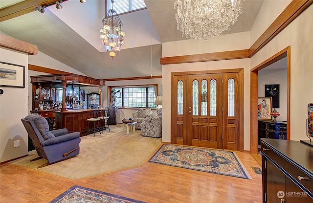 foyer with bar area, an inviting chandelier, light hardwood / wood-style flooring, and high vaulted ceiling