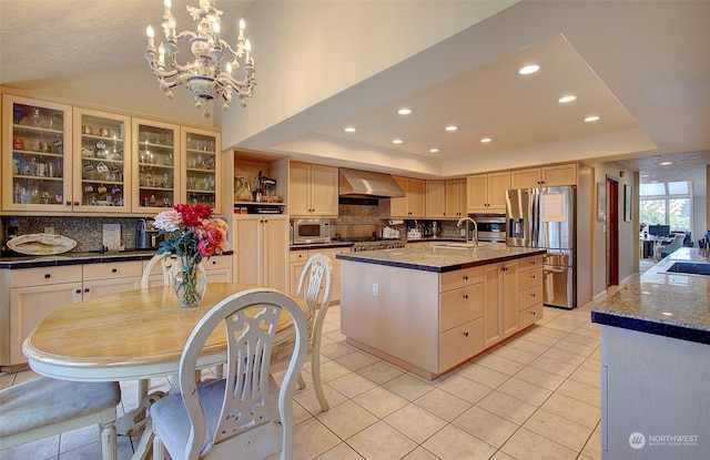 kitchen featuring an island with sink, backsplash, ventilation hood, stainless steel appliances, and a notable chandelier