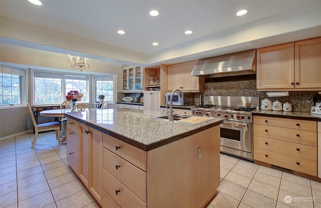 kitchen with decorative backsplash, an island with sink, light tile patterned floors, high end range, and wall chimney range hood