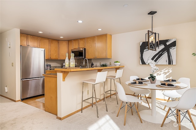 kitchen featuring a kitchen bar, sink, decorative light fixtures, kitchen peninsula, and stainless steel appliances