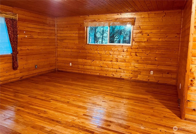 empty room with wood ceiling, light wood-type flooring, and wooden walls