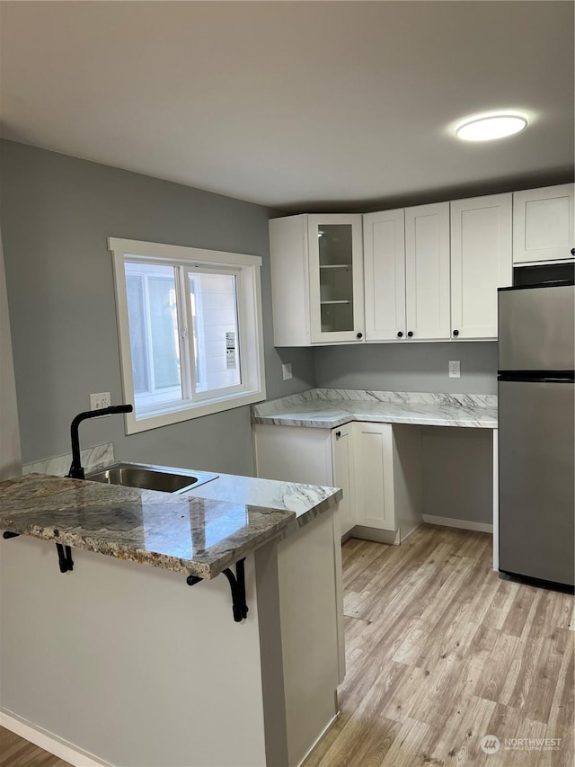 kitchen with stainless steel fridge, light stone counters, white cabinets, a breakfast bar, and sink