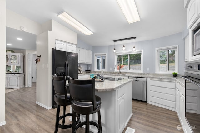 kitchen with light wood-type flooring, a breakfast bar, black appliances, white cabinets, and a kitchen island