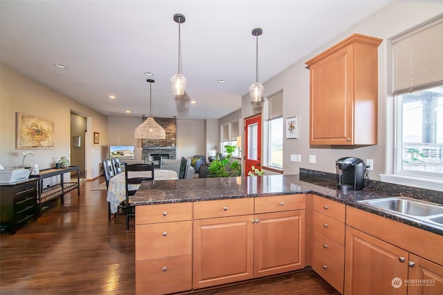 kitchen with kitchen peninsula, hanging light fixtures, dark wood-type flooring, and a stone fireplace