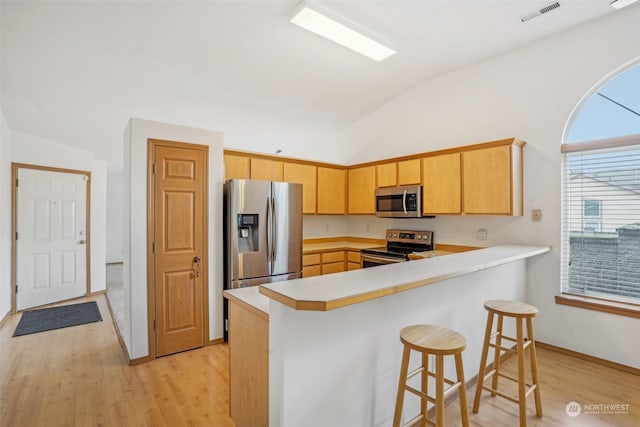 kitchen featuring kitchen peninsula, appliances with stainless steel finishes, light hardwood / wood-style flooring, and lofted ceiling