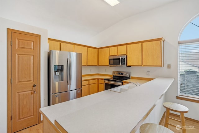 kitchen featuring kitchen peninsula, appliances with stainless steel finishes, light wood-type flooring, vaulted ceiling, and sink