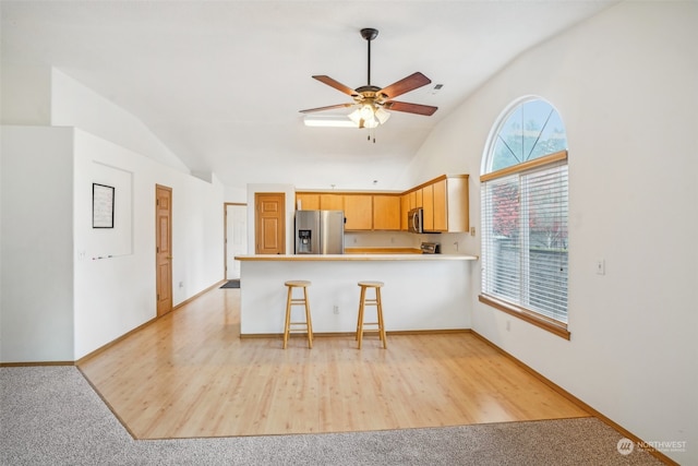 kitchen featuring lofted ceiling, light brown cabinetry, kitchen peninsula, and appliances with stainless steel finishes