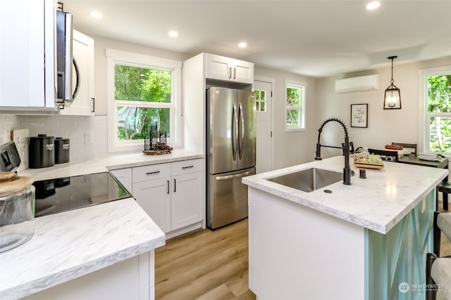 kitchen featuring a kitchen island with sink, sink, white cabinetry, hanging light fixtures, and appliances with stainless steel finishes