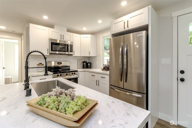 kitchen with stainless steel appliances, white cabinets, light stone counters, and backsplash