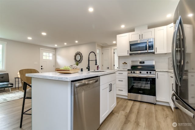 kitchen featuring appliances with stainless steel finishes, light hardwood / wood-style floors, white cabinets, a kitchen island with sink, and sink