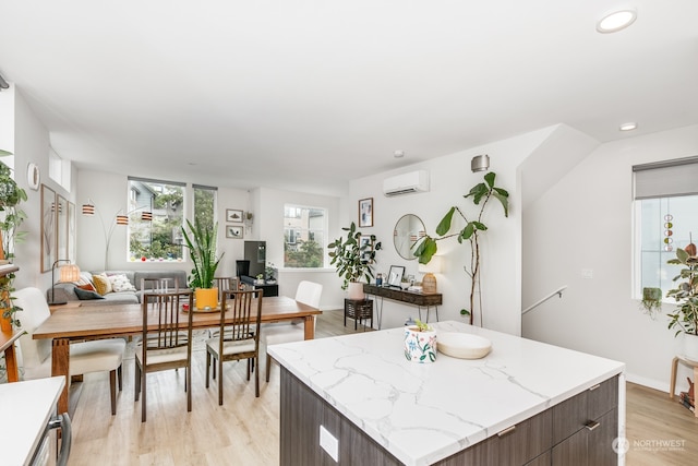 kitchen featuring a kitchen island, dark brown cabinets, light stone countertops, light hardwood / wood-style floors, and an AC wall unit