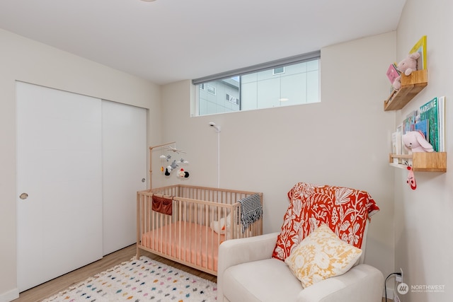 bedroom with a crib, light hardwood / wood-style flooring, and a closet