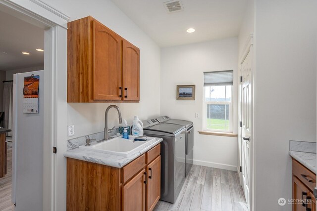 laundry area featuring washing machine and clothes dryer, light wood-type flooring, cabinets, and sink