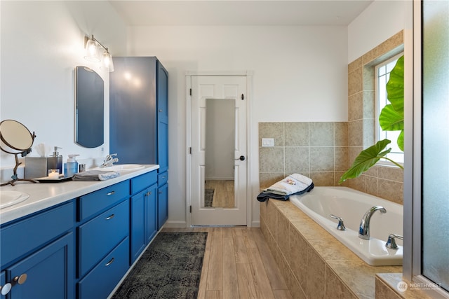 bathroom featuring wood-type flooring, tiled bath, and vanity