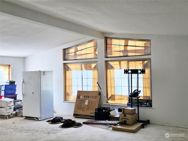 interior space featuring a textured ceiling, beamed ceiling, concrete flooring, and white refrigerator