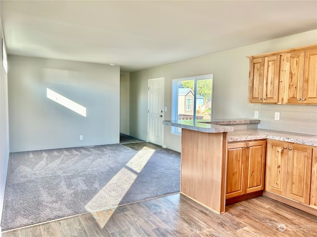 kitchen featuring kitchen peninsula, light hardwood / wood-style flooring, a skylight, and tasteful backsplash