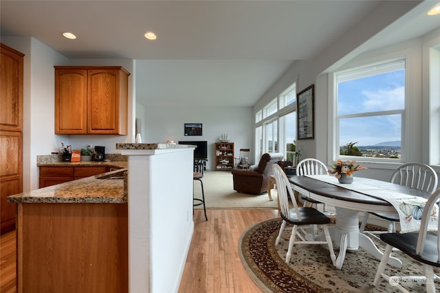 kitchen with vaulted ceiling, light wood-type flooring, kitchen peninsula, and dark stone counters