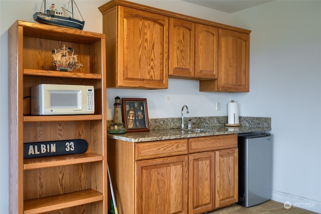 kitchen featuring stainless steel fridge, dark stone countertops, and sink