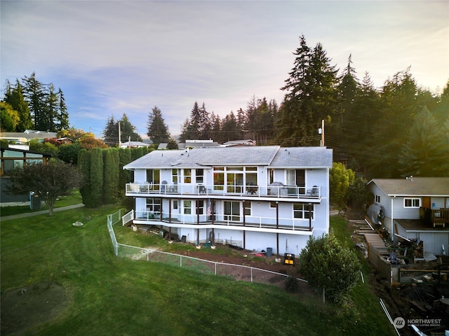 back house at dusk featuring a lawn and a balcony