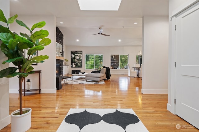 foyer entrance with a skylight, a large fireplace, light wood-type flooring, and ceiling fan